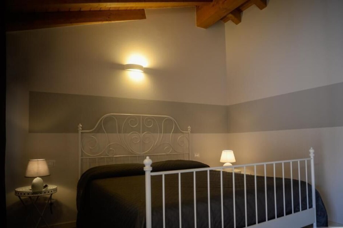 A bedroom with a metal bed frame, a bedside table with a lamp, and a wall-mounted light fixture.