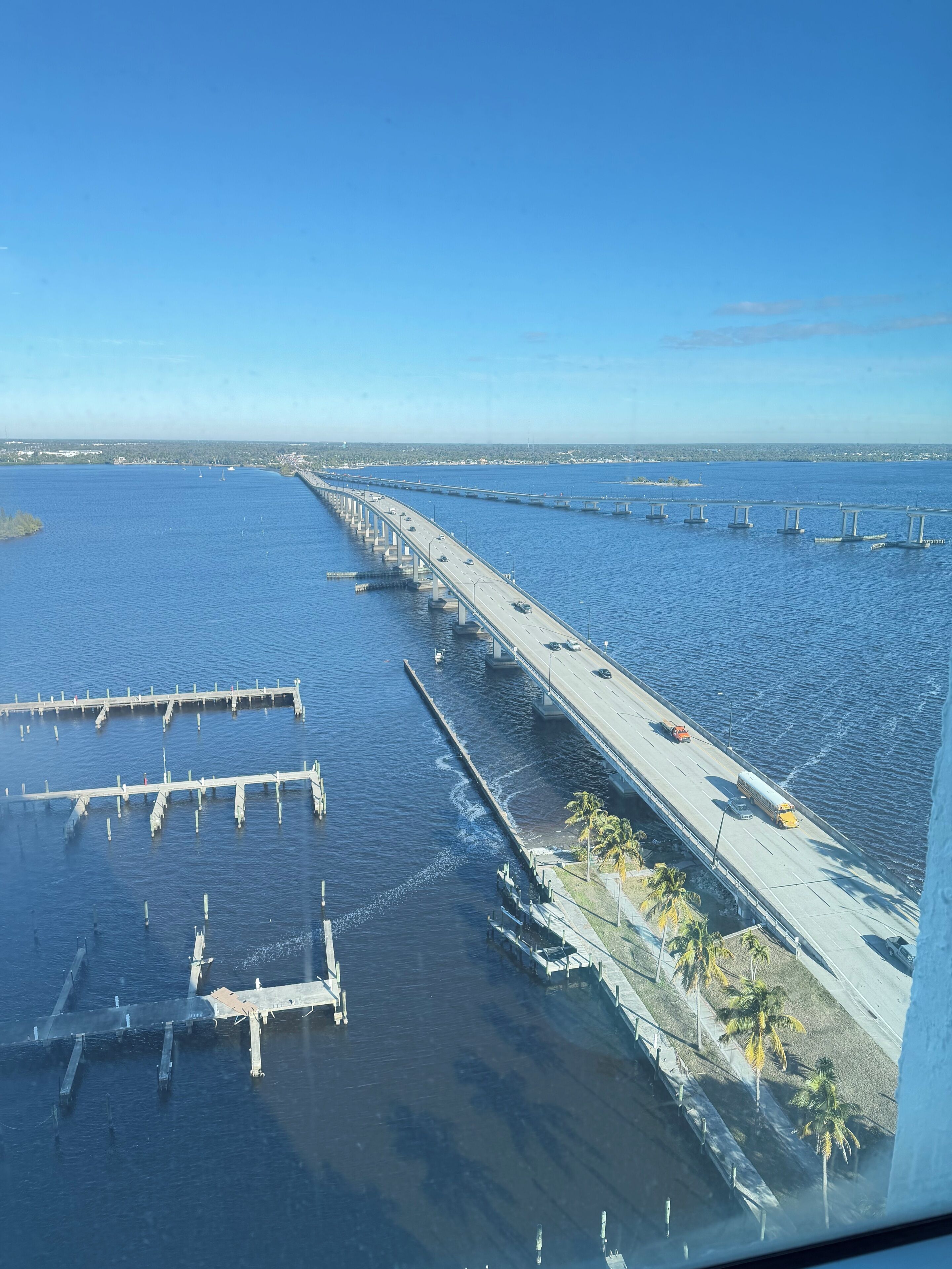 Un puente largo sobre el agua, con varios pilares, una carretera con vehículos y un cielo despejado.