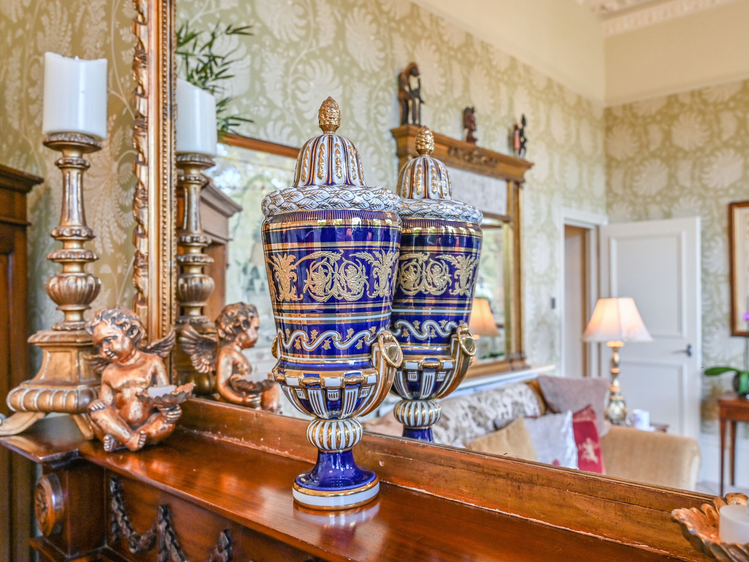 Un comò in legno con vasi azzurri e dorati decorati, uno specchio e oggetti ornamentali.