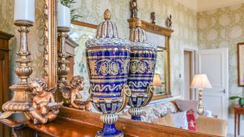 Un comò in legno con vasi azzurri e dorati decorati, uno specchio e oggetti ornamentali.