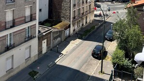 Ein mehrstöckiges Gebäude mit einer Fassade aus Backstein und Naturstein, eine Straße mit Autos und einem strahlend blauen Himmel.