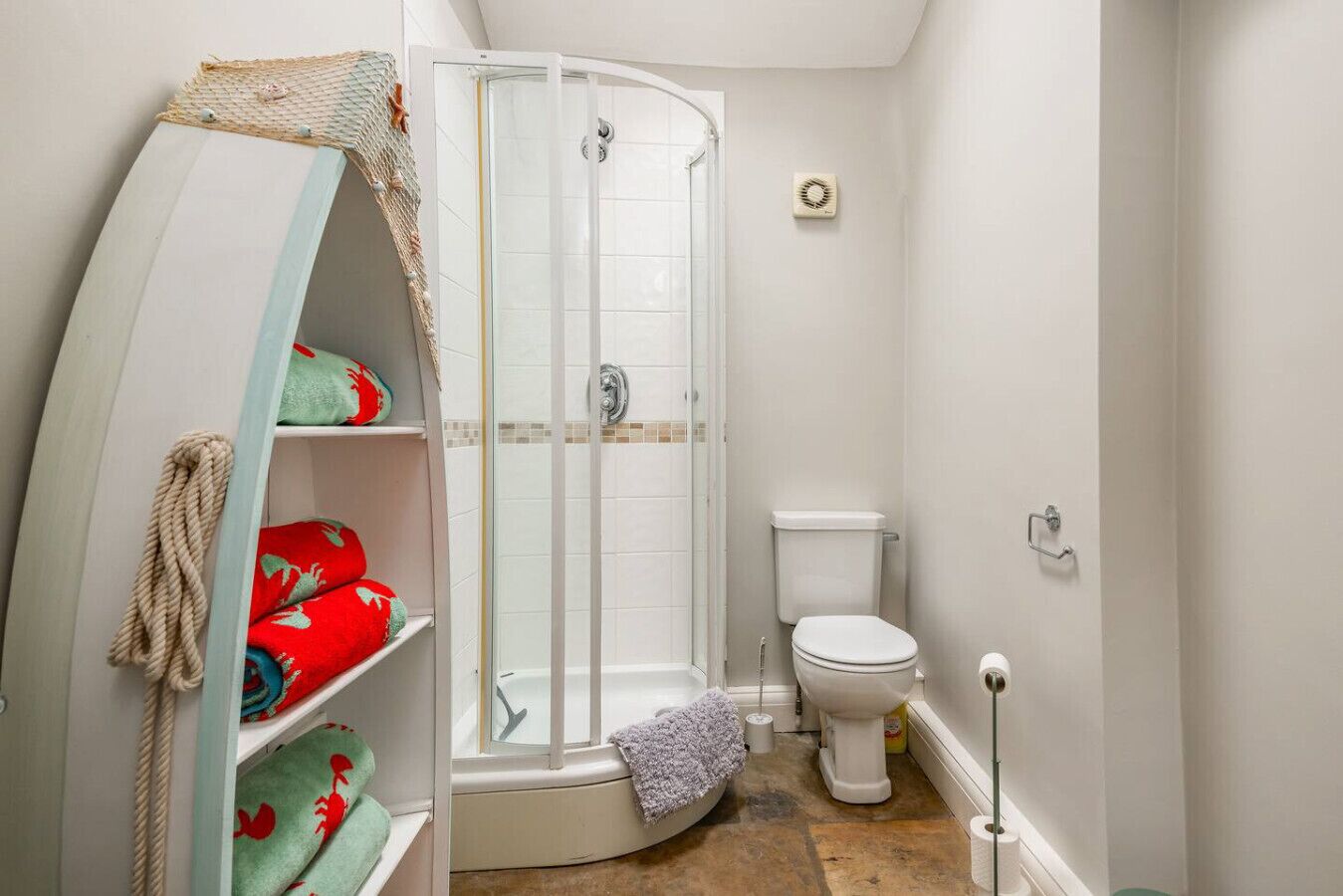 Une salle de bain avec une douche à parois de verre, des toilettes et une étagère avec des serviettes.