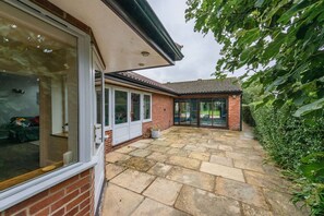 Une maison en briques avec un patio, une porte vitrée et un petit jardin.