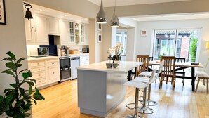 Une cuisine moderne avec des meubles blancs, un îlot central et un coin repas comprenant des chaises et une table en bois.