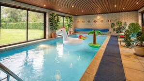 Une piscine intérieure avec un plafond en bois, un flotteur en forme de licorne blanche gonflable et des plantes en pot.