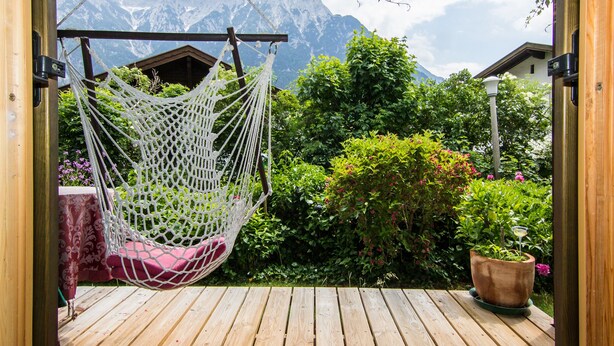 A wooden deck with a white hanging chair and a potted plant. - Landhaus Albrecht - Holiday Apartment 01 - with 2 terraces and fireplace (50 m²) (Mittenwald)