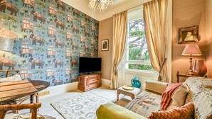 Una habitación con papel tapiz estampado, televisor, mesa de madera, sofá y ventana con cortinas.