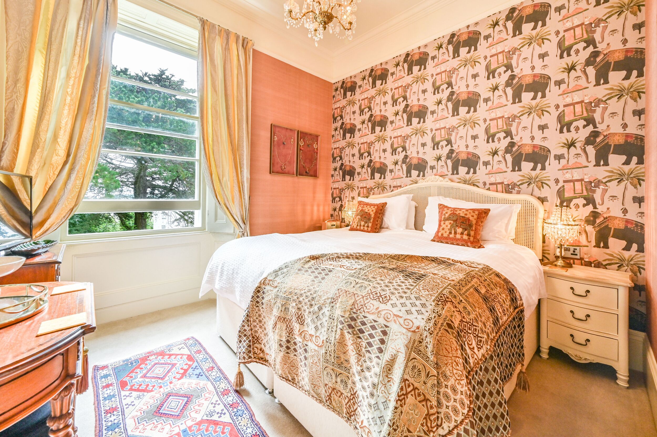 A bedroom with a large bed, a nightstand, a dresser, and a window with curtains.