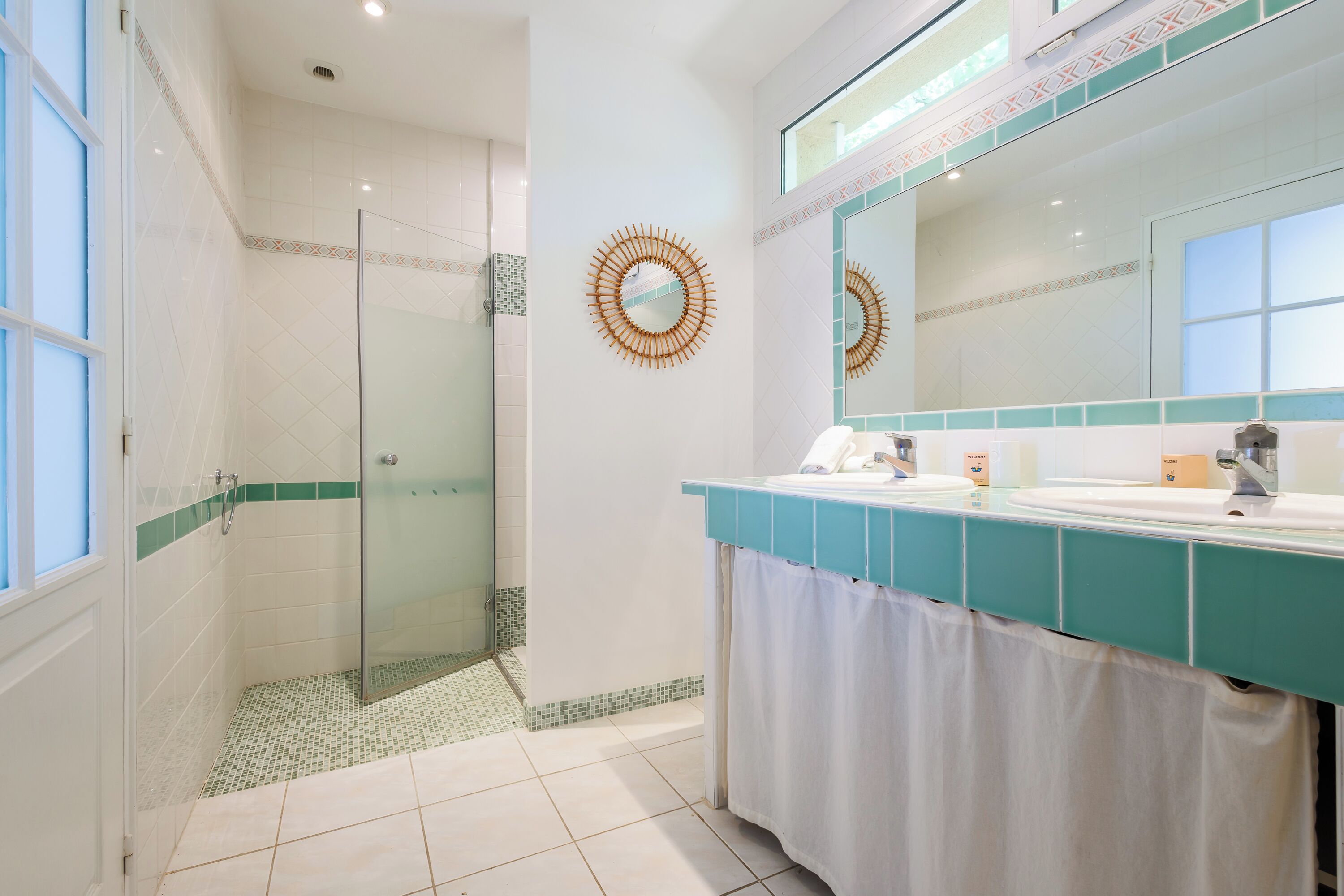 A modern bathroom with a glass-enclosed shower, a large mirror, and a teal-colored vanity.