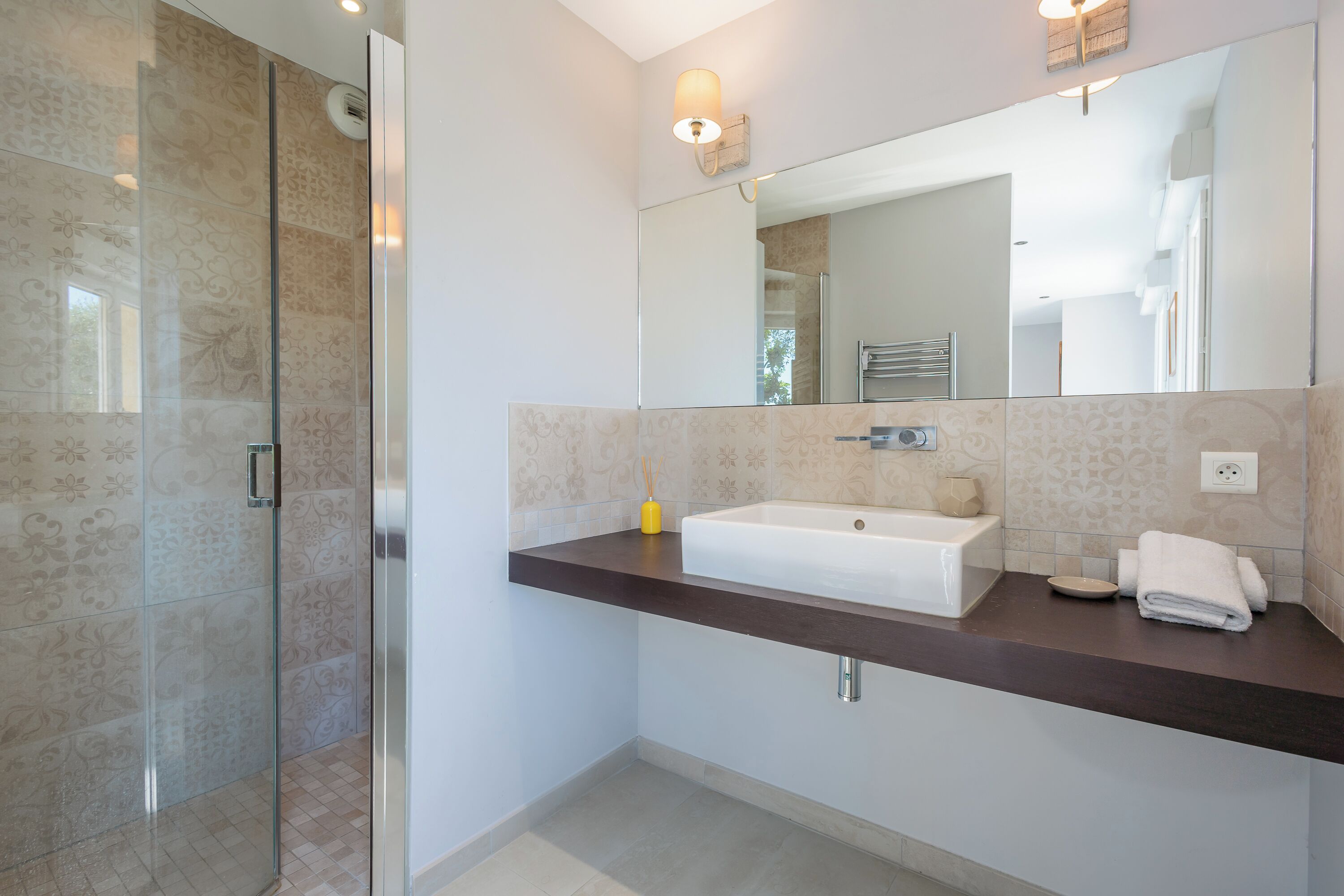 Une salle de bain moderne avec une douche à l’italienne en verre, un lavabo blanc et un plan de toilette foncé.