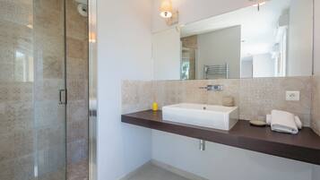 Une salle de bain moderne avec une douche à l’italienne en verre, un lavabo blanc et un plan de toilette foncé.
