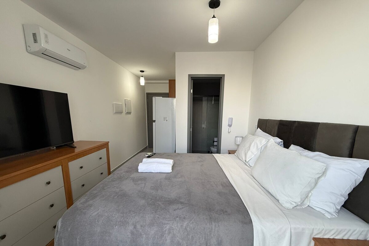 Ein Hotelzimmer mit Bett, Fernseher auf einer Holzkommode, einer Tür zu einem Badezimmer und einer Deckenleuchte.
