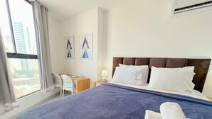 Ein Hotelzimmer mit einem Bett, einem Schreibtisch, zwei Stühlen, einer Lampe und einem Fenster mit Blick auf die Stadt.
