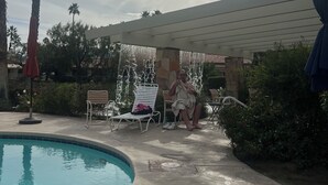 Ein Poolbereich mit Liegestühlen, Palmen und einer überdachten Sitzgelegenheit.
