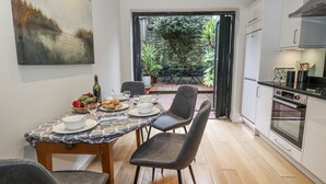 A modern kitchen with white cabinets, a built-in oven, and a dining area with a table set for four. - Harbourside (Weymouth)