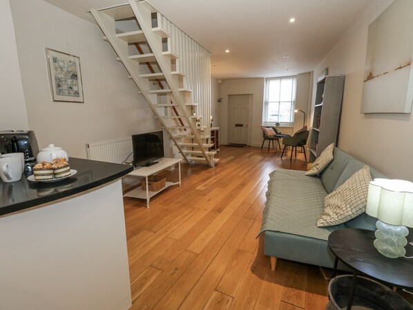 Ein modernes Wohnzimmer mit Holzboden, einer Couch, einem Fernseher, einem Couchtisch und einer Treppe.
