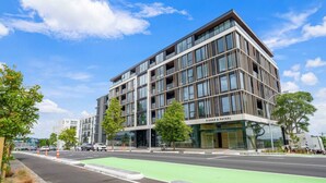 En moderne bygning med en glasfacade, der er markeret med "FISHER & PAYKEL", med en cykelsti og træer i forgrunden.