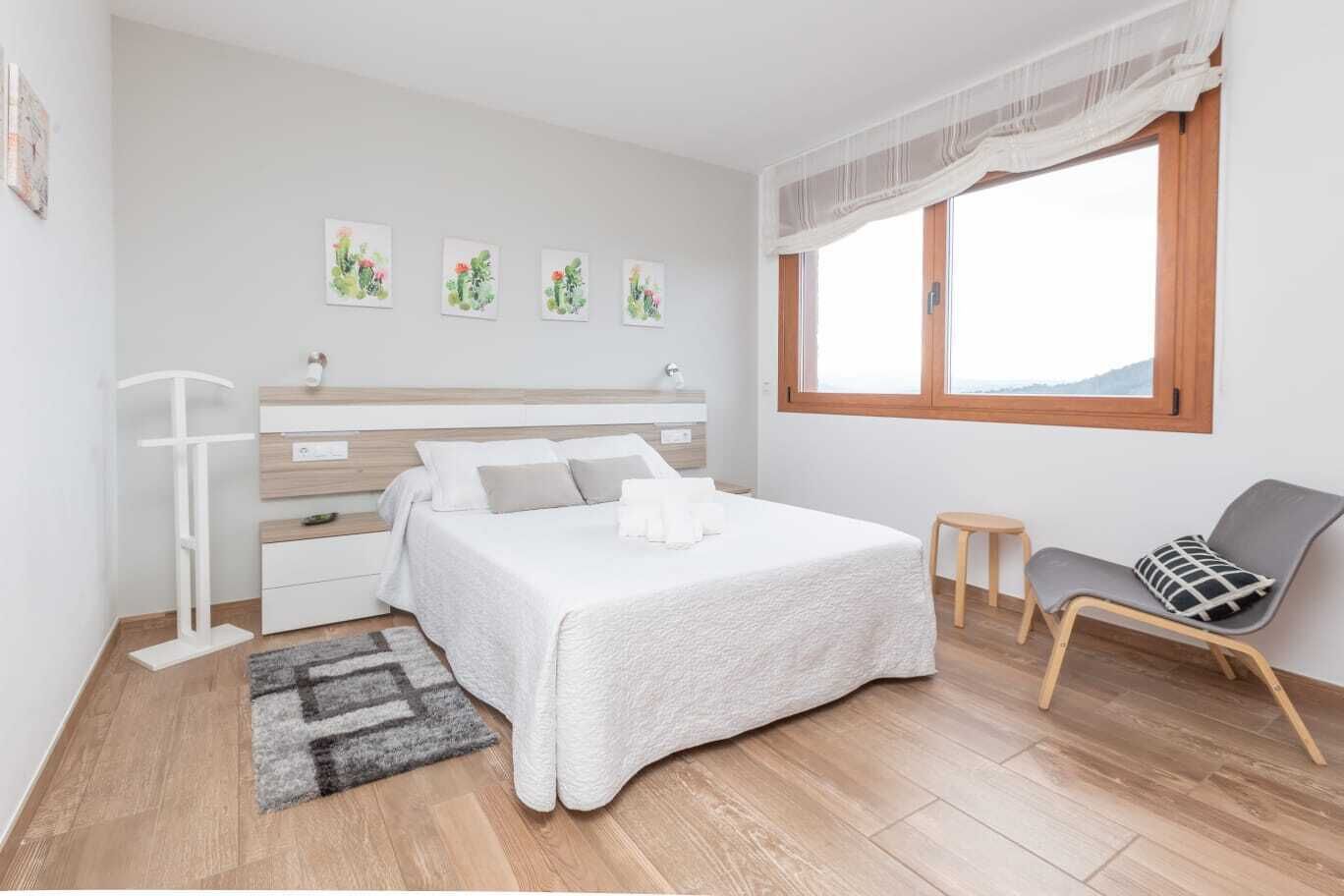A bedroom with a bed, bedside table, chair, and artwork on the wall.