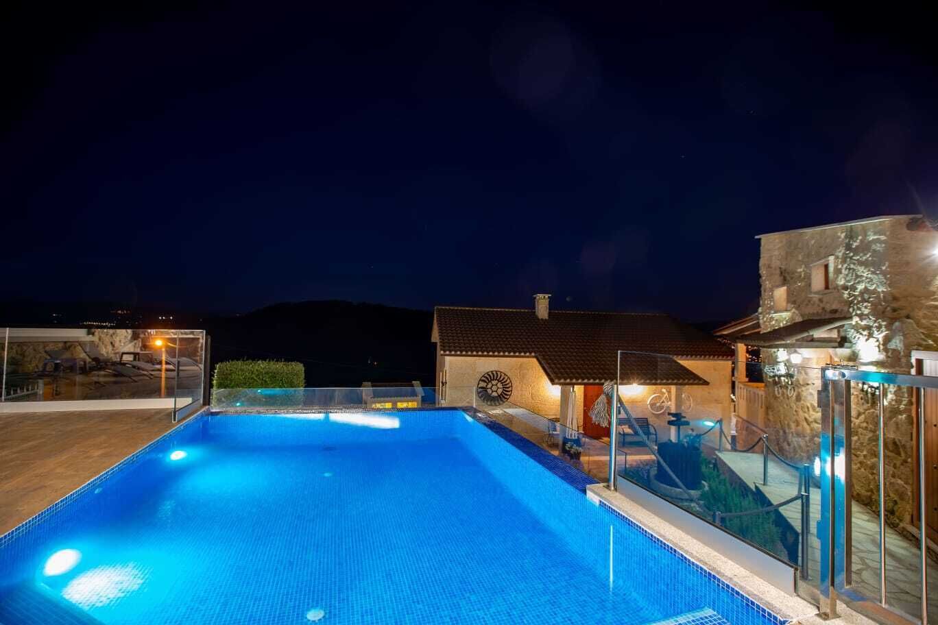 A swimming pool with a glass barrier, a stone building, and a mountain in the background.