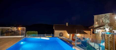 A swimming pool with a glass barrier, a stone building, and a mountain in the background.