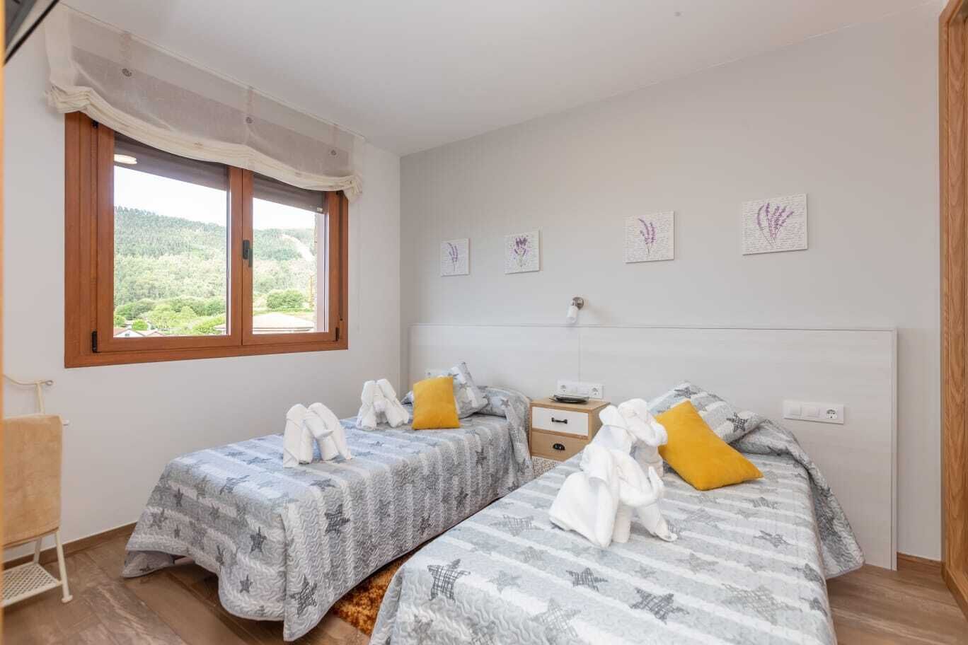 A bedroom with two beds, a window with a view, and a small bedside table.