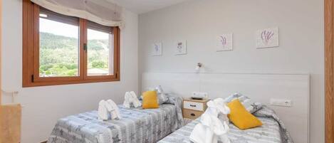A bedroom with two beds, a window with a view, and a small bedside table.