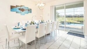 Ein Essbereich mit Glastür zum Pool, weißen Stühlen und einer Kristallleuchter.