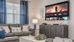 Ein modernes Wohnzimmer mit einem grauen Sofa, einem weißen Couchtisch und einem Fernseher, der 'Star Wars: Mandalorian' zeigt.