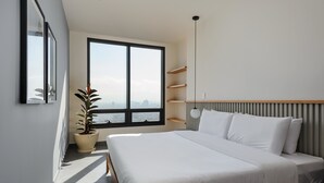 Quarto moderno com uma janela grande, uma cama, um vaso de planta e prateleiras embutidas.