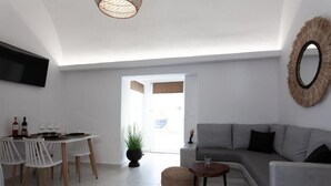Ein modernes Wohnzimmer mit einem grauen Sofa, einem Esstisch mit Stühlen, einem an der Wand befestigten Fernseher und einem großen Spiegel.