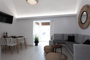 Uma sala de estar moderna com um sofá cinzento, uma mesa de jantar com cadeiras, uma TV fixada na parede e um espelho grande.