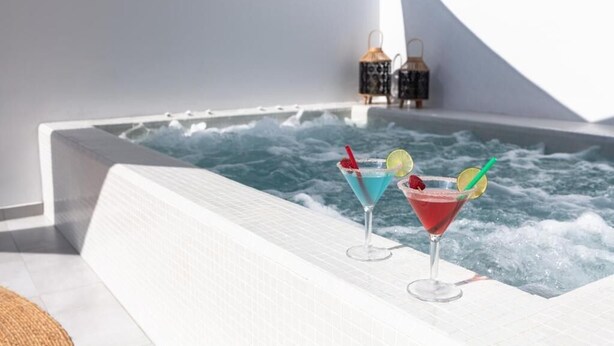 Ein Whirlpool mit zwei Cocktails, einer weißen Fliesenwand und zwei Laternen.