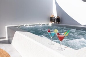 Una vasca idromassaggio con due cocktail, una parete rivestita di piastrelle bianche e due lanterne.