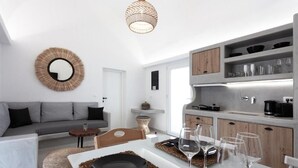 Ein modernes Wohnzimmer mit einem grauen Sofa, einem Esstisch mit Tellern und Gläsern sowie einer Küchenzeile mit Holzschränken und einer Pendelleuchte.