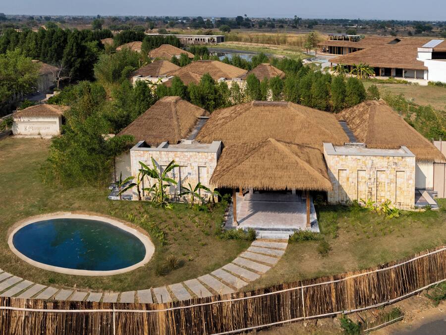 Un complexe hôtelier comprenant plusieurs bungalows aux toits de chaume, une piscine et un sentier en pierre.