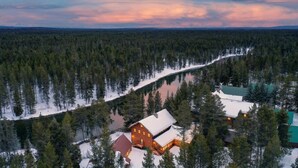 Een chalet omringd door dicht bos en een met sneeuw bedekte pad dat naar een meer leidt.