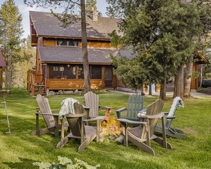Une cabane en rondins avec un foyer et des fauteuils Adirondack dans la cour.