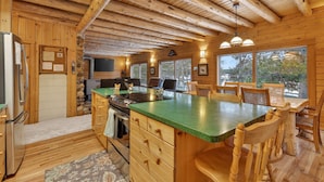 Een rustiek cabin interieur met een houten eethoek, een keuken met een groen aanrecht en een stenen openhaard.