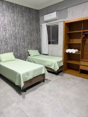 A room with two beds, a wooden wardrobe, and an air conditioning unit. - Arbo Belém Quartos padrão Anfitrião 360 (Belém)