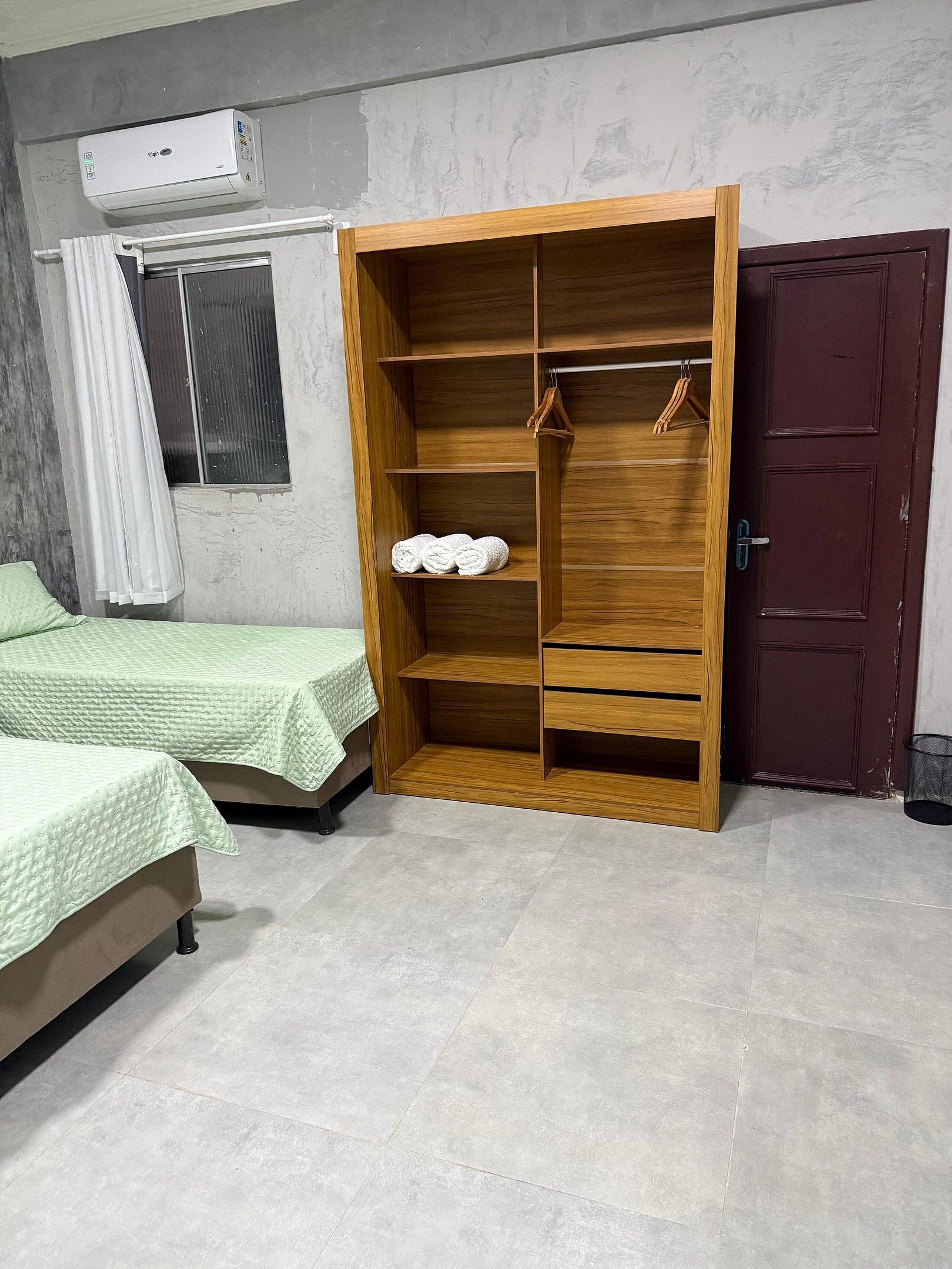Ein Schlafzimmer mit zwei Betten, einem Holzschrank mit Kleiderhaken, einem Fenster mit Vorhängen und einer Tür.