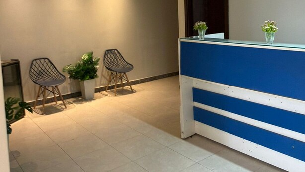 A reception area with a blue counter, two chairs, a potted plant, and an air conditioning unit on the wall. - Arbo Belém Quartos padrão Anfitrião 360 (Belém)