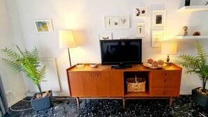 Ett modernt vardagsrum med ett TV-bord i trä, en platt-TV, två golvlampor och inramade botaniska tryck på väggen.