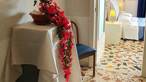 Ett hotellrum med en säng, ett bord med en blomsteruppsättning, en stol och en väggmonterad lampa.