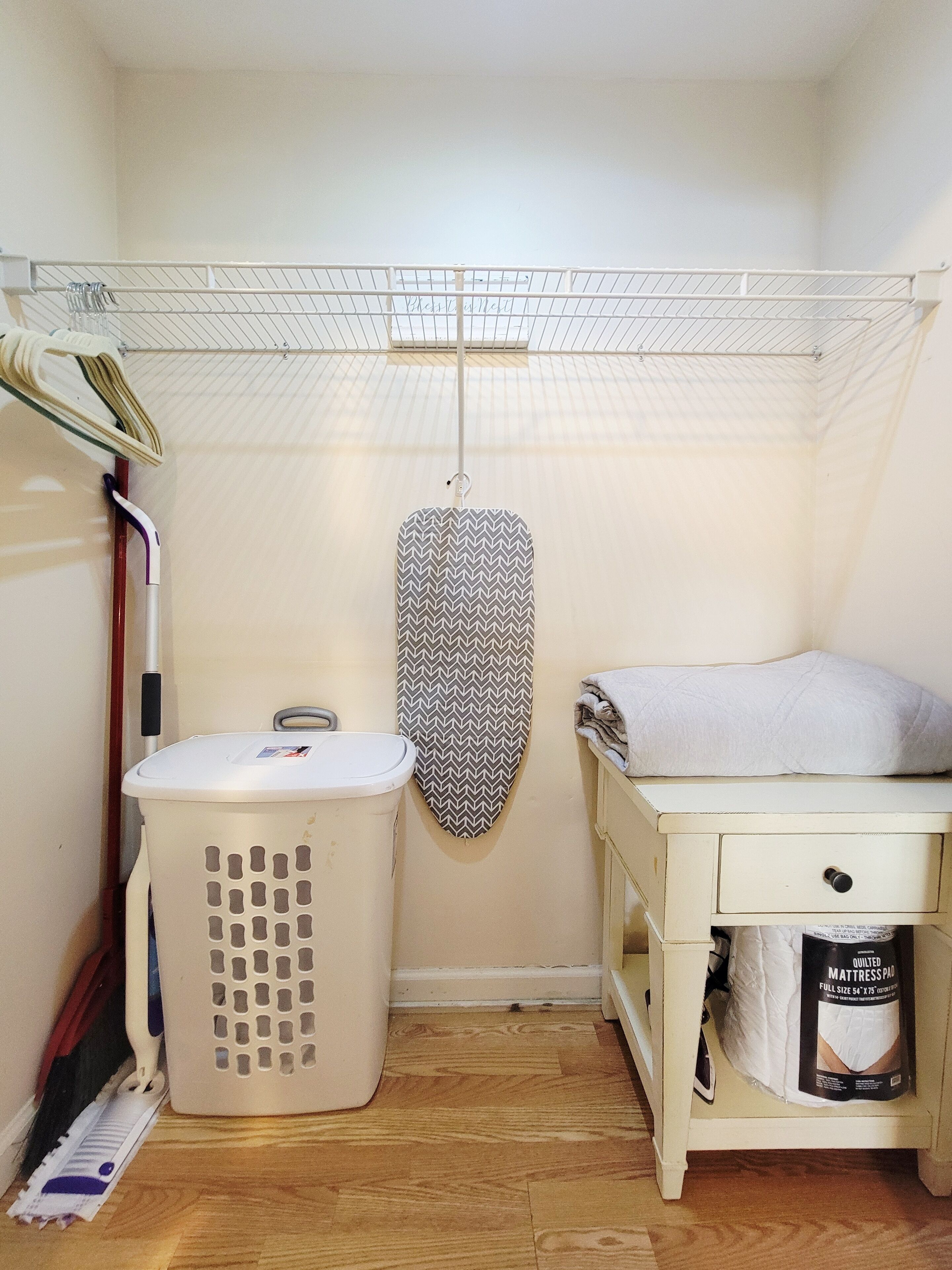 A laundry room with a washing machine, a drying rack, and a mattress pad.