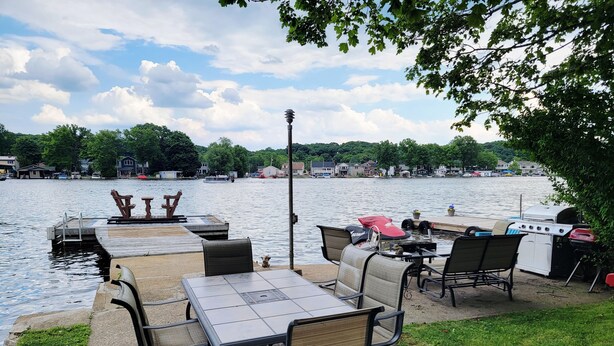 A lakeside patio with a table and chairs, a grill, and a dock extending into the water. - 1 Bed 1 bath Lakefront Apartment in Lake Hopatcong, NJ w/ lake access and kayaks (Jefferson)