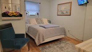 A bedroom with a bed, a chair, a TV mounted on the wall, and a window with curtains. - 1 Bed 1 bath Lakefront Apartment in Lake Hopatcong, NJ w/ lake access and kayaks (Jefferson)