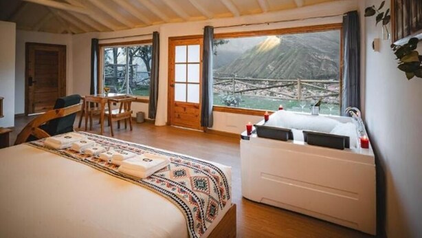 Een slaapkamer met een groot bed, een bureau en uitzicht op een bergachtig landschap door een raam.