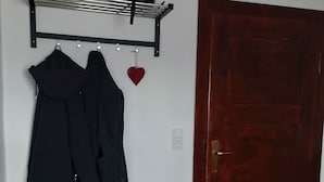 A room with a wooden floor, a black coat rack with a helmet and a heart-shaped decoration, a wooden door, and a mat with shoes. - Vacation/ mechanic apartment Nikki (Argenthal)