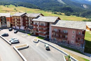 A multi-story residential building with balconies, a parking lot, and a mountainous backdrop. - 10m from ski slopes, Ground floor, view ski slopes, terrace, tv, ski locker, 27m², Val Cenis (Termignon)