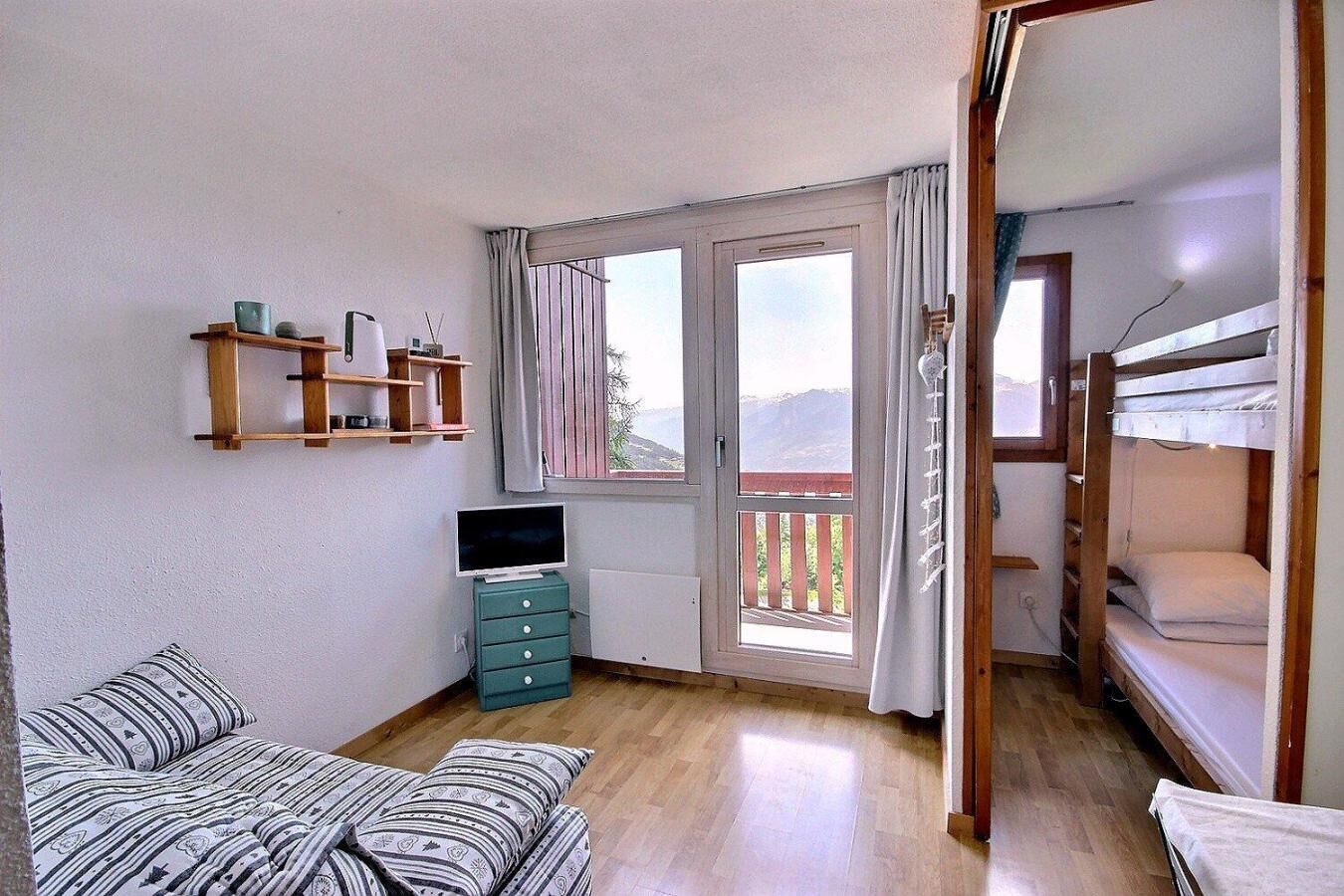 Ein Zimmer mit einer Couch, einem Fernseher, einem Schminktisch, einem Etagenbett und einem Balkon mit Blick.